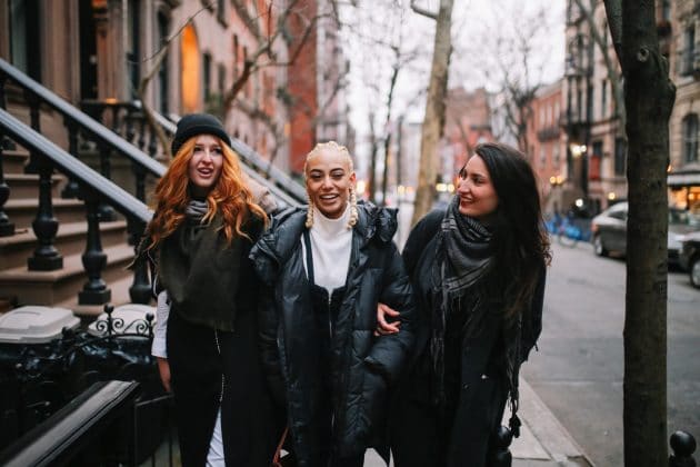 Três amigas sorridentes caminhando em rua urbana ao entardecer