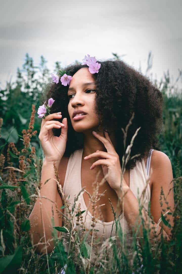  Mulher negra de cabelo crespo, castanho escuro, na altura dos ombros, com algumas flores lilás
