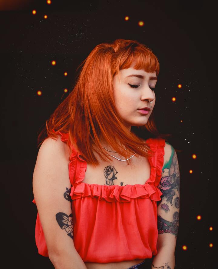 Mulher ruiva cheia de tatuagens posando para foto com os olhos fechados