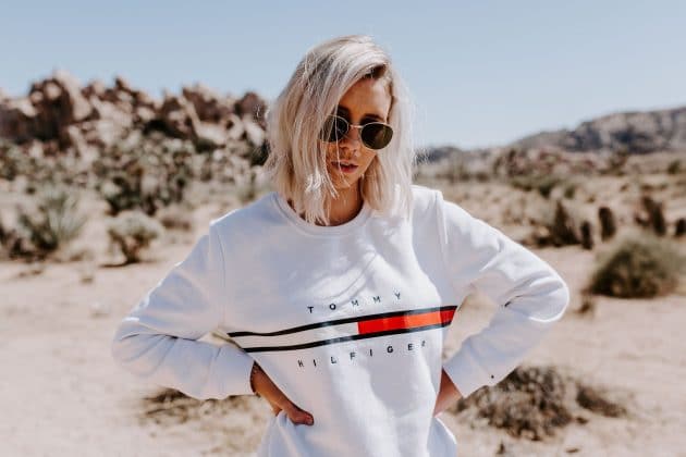 Mulher com cabelo loiro e óculos redondos, vestindo moletom Tommy Hilfiger no deserto