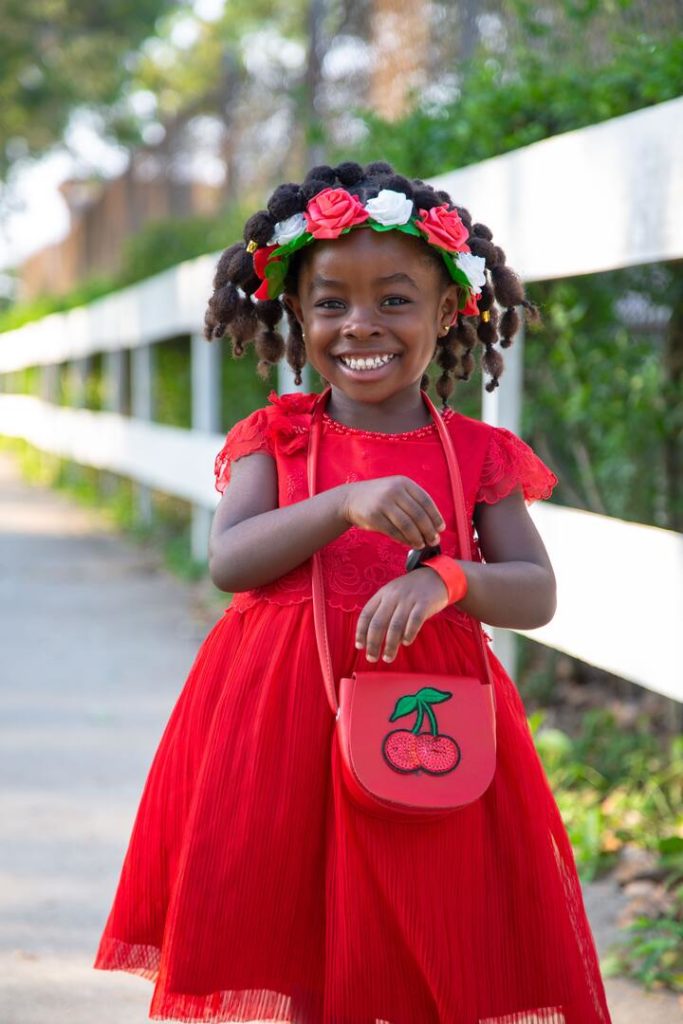 menina sorrindo usando um vestido vermelho com tranças nos cabelos