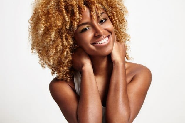 Mulher radiante com cabelo afro loiro sorrindo para a câmera