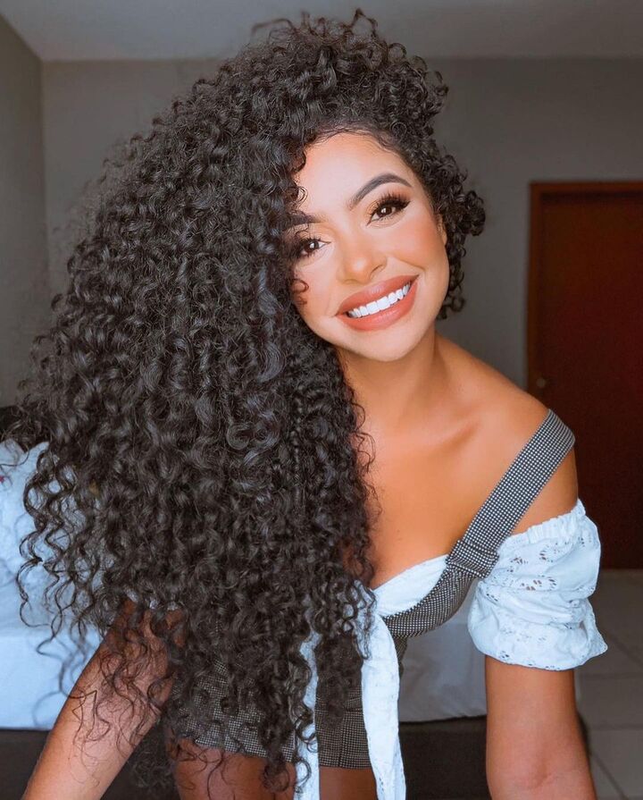 mulher de cabelos cacheados sorrindo para a foto