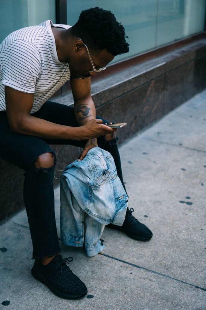 homem negro sentado na mureta mexendo no celular