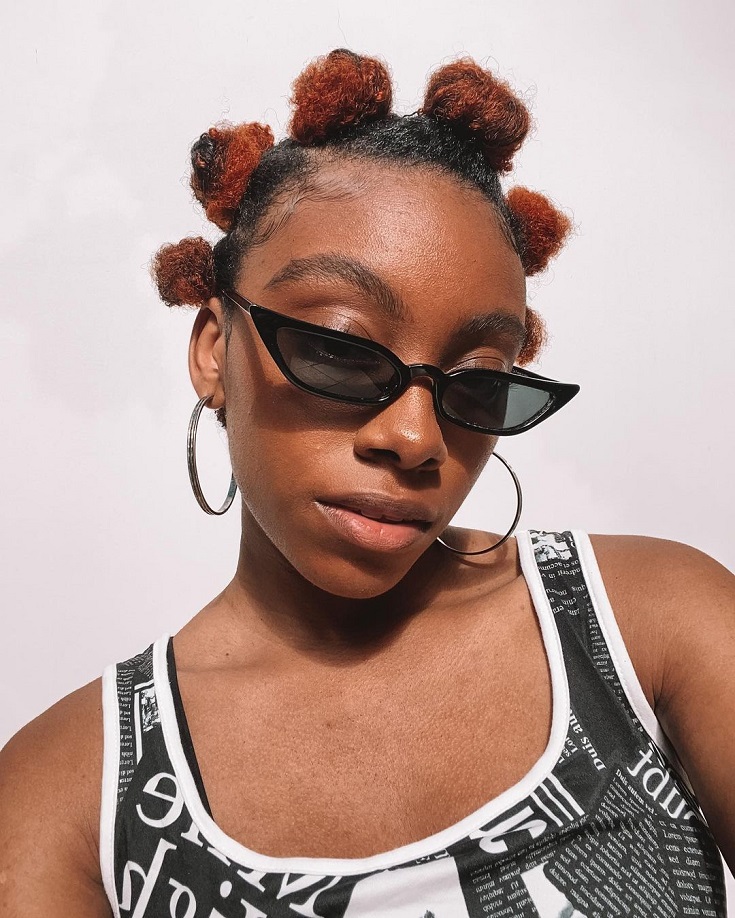 Mulher negra de cabelo crespo curto, com o penteado Bantu Knots (vários coquinhos no cabelo)