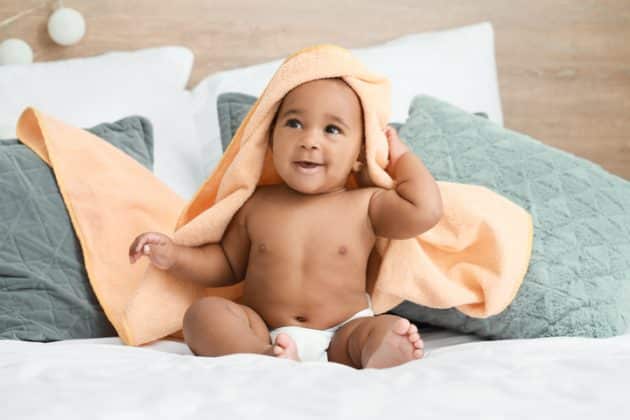 bebezinho sentado na cama, de fralda e com uma toalha na cabeça