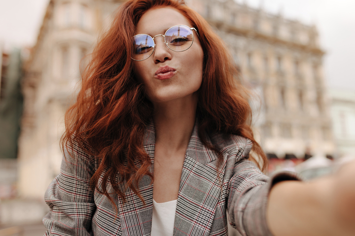  Mulher mandando um beijinho para a foto com os cabelos ruivos e usando óculos de sol