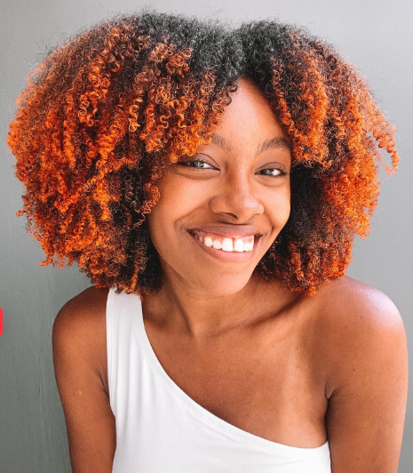  Mulher negra de cabelos avermelhados sorrindo para a foto