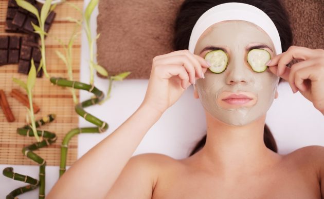 Mulher relaxando com máscara facial de argila e pepinos nos olhos
