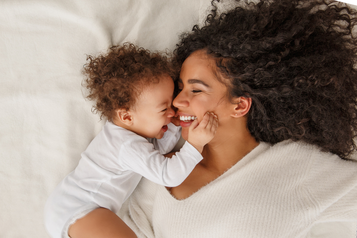 mãe deitada na cama sorrindo com seu bebê ao lado