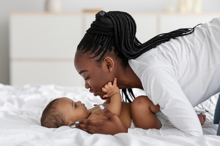 mãe beijando seu bebê que está deitado na cama