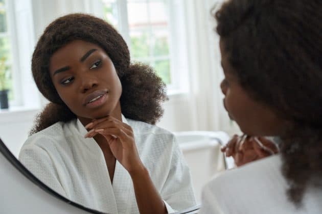 Mulher negra em frente ao espelho analisando o seu tipo de pele