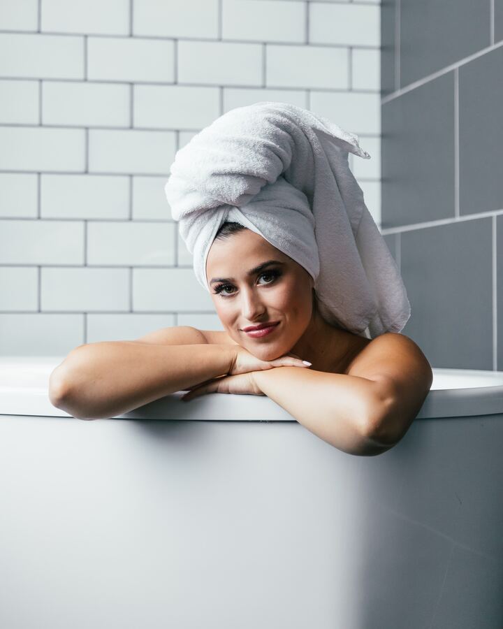  Mulher dentro da banheira tomando banho com toalha enrolada no cabelo