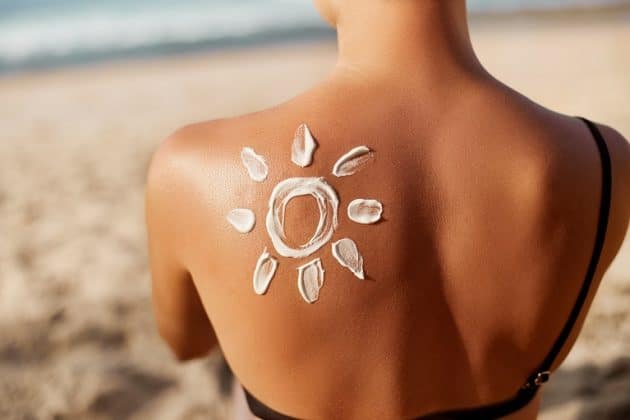 Mulher branca na praia, com o desenho de um sol nas costas, feito com protetor solar