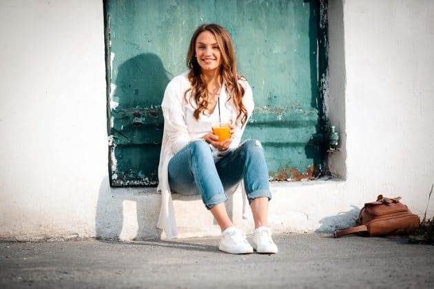 Mulher com roupas de inverno tomando um suco de laranja. Vitamina C evita o ressecamento da pele no frio