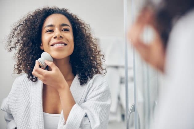 Mulher negra de cabelo cacheado, fazendo uma rotina de skincare com esponja facial polvo