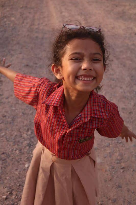 Menininha sorrindo, com os olhos fechados e braços abertos