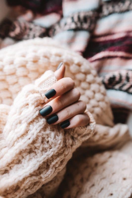 A imagem mostra uma mão feminina com a unha esmaltada de preto