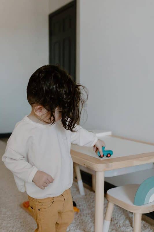 Menininho de cabelo liso, longo, brincando de carrinho em cima da mesa