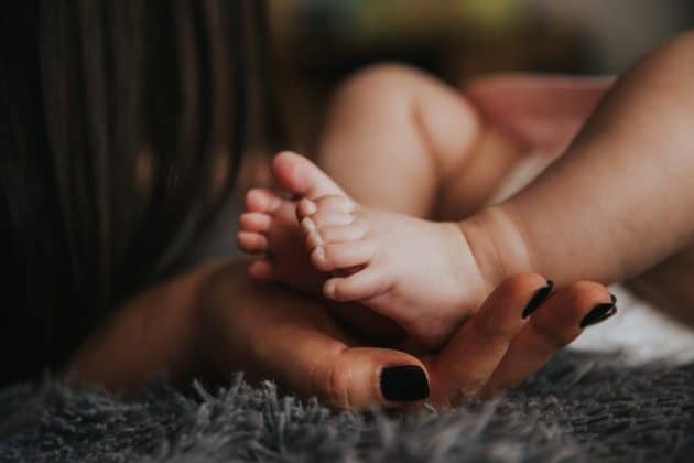 Baby blues X depressão pós-parto. A imagem mostra uma mão feminina, com unhas pintadas de preto, segundo os pézinhos de um bebê