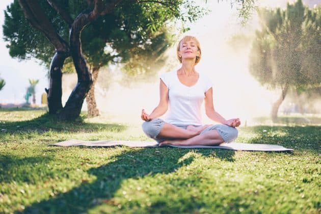 Mulher mais velha, de cabelos grisalhos, praticando meditação em um parque