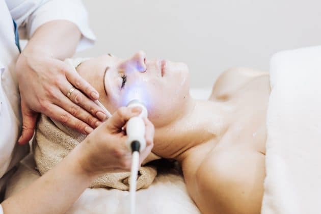 A imagem mostra uma mulher branca, deitada em uma maca estética, fazendo tratamento a laiser para vermelhidão no rosto