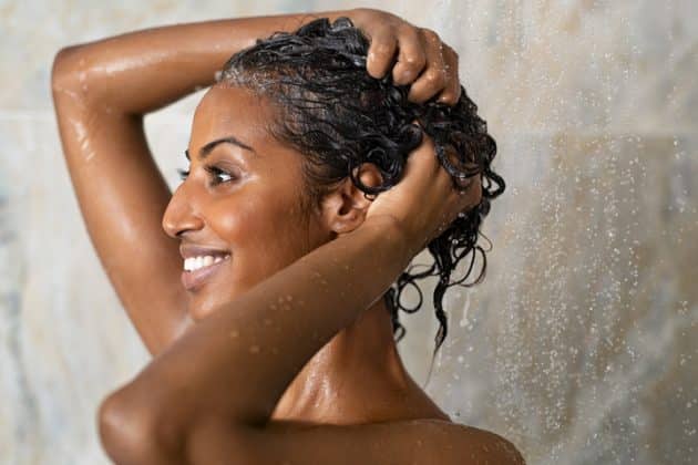 Mulher negra lavando o cabelo no banho, para evitar a foliculite no couro cabeludo
