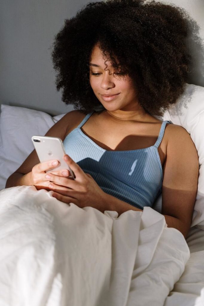 mulher negra deitada na cama mexendo no celular