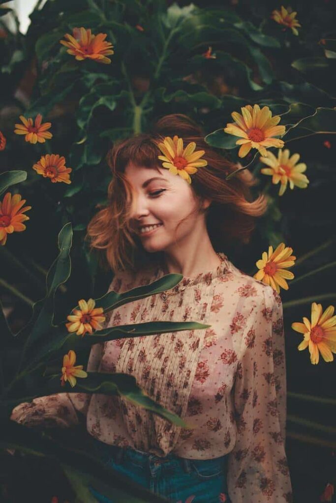 Mulher jovem de cabelo curto, ruivo e liso, no meio de umas flores amarelas