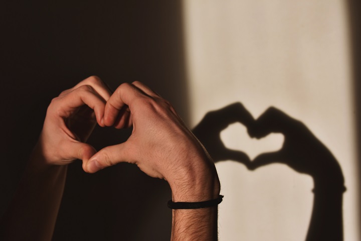  mãos fazendo a forma de um coração e projetando a sombra na parede. Representatividade do amor romântico
