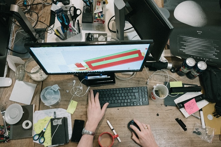 Mesa de trabalho desordenada com monitor mostrando gráfico, teclado e itens diversos