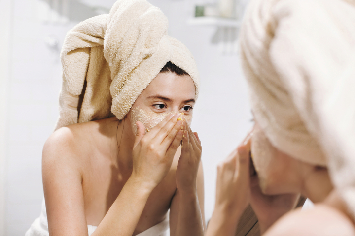Mulher fazendo esfoliação no rosto em frente ao espelho