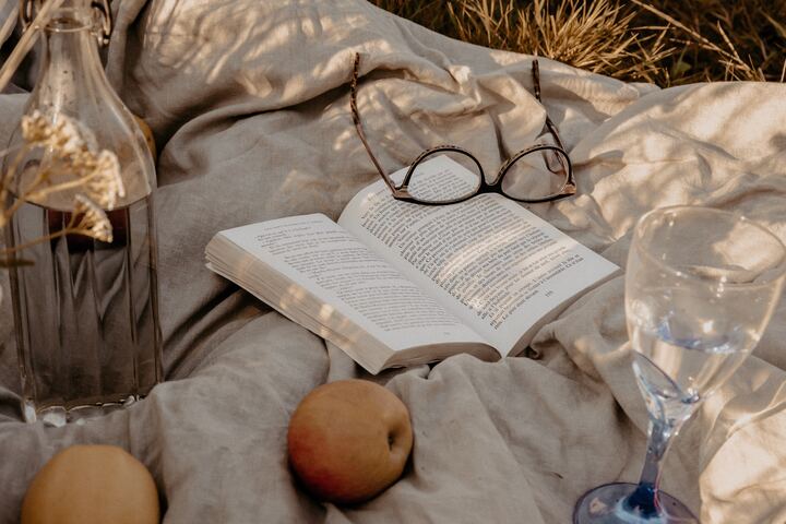  livro aberto sobre cobertor junto com uma maça e óculos