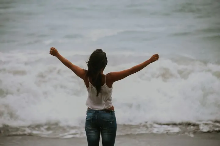  mulher de costas para a foto com os braços abertos em frente ao mar