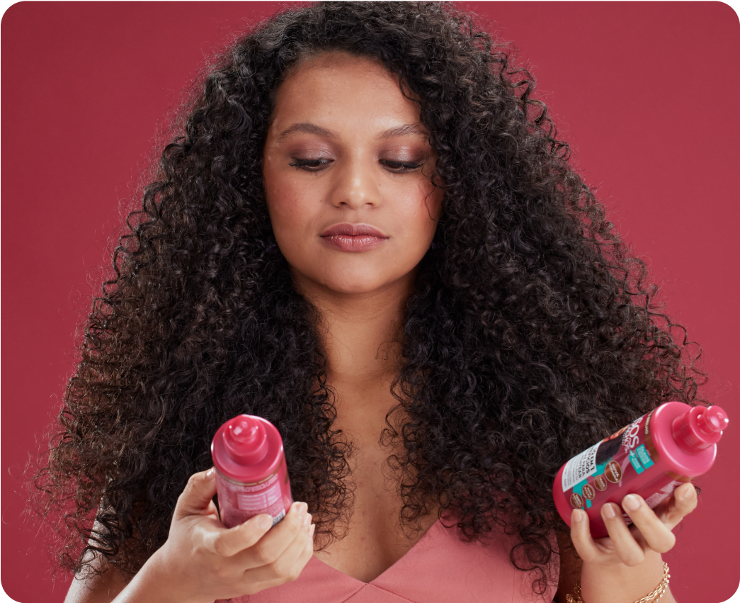 mulher negra de cabelos longos e cacheados olhando para dois produtos da Salon Line