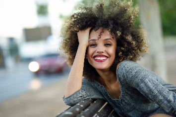 Mulher sorridente com cabelo cacheado, exibindo autoestima e alegria em ambiente urbano, perfeita para retratar beleza e empoderamento feminino.